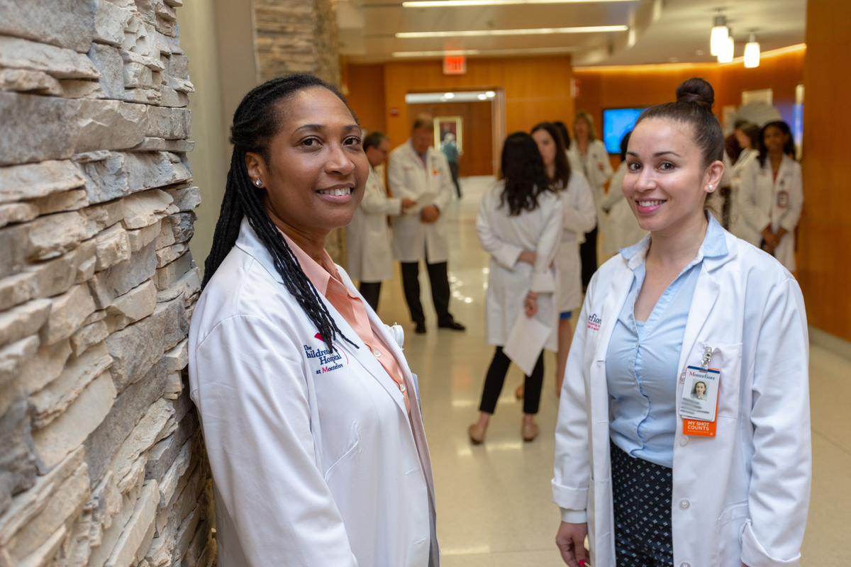 two female pharmacists in a hallway with a group of pharmacist in the background